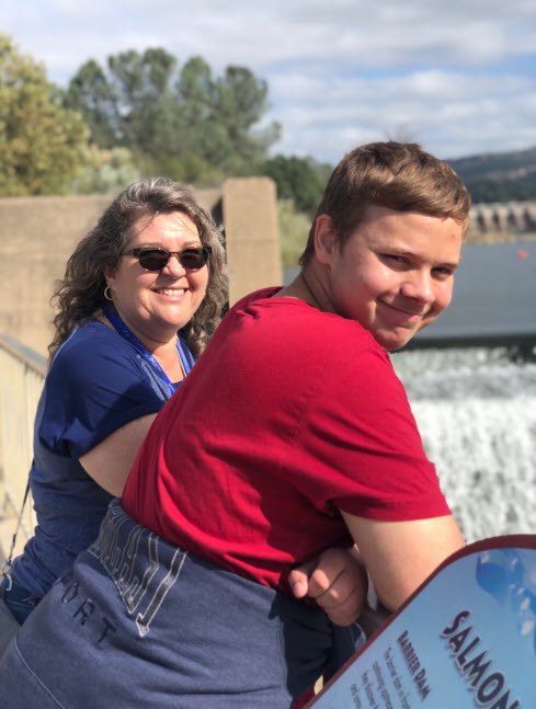 Image of a female staff member with a transition aged student smiling at the camera in front of the Oroville Salmon Hatchery.